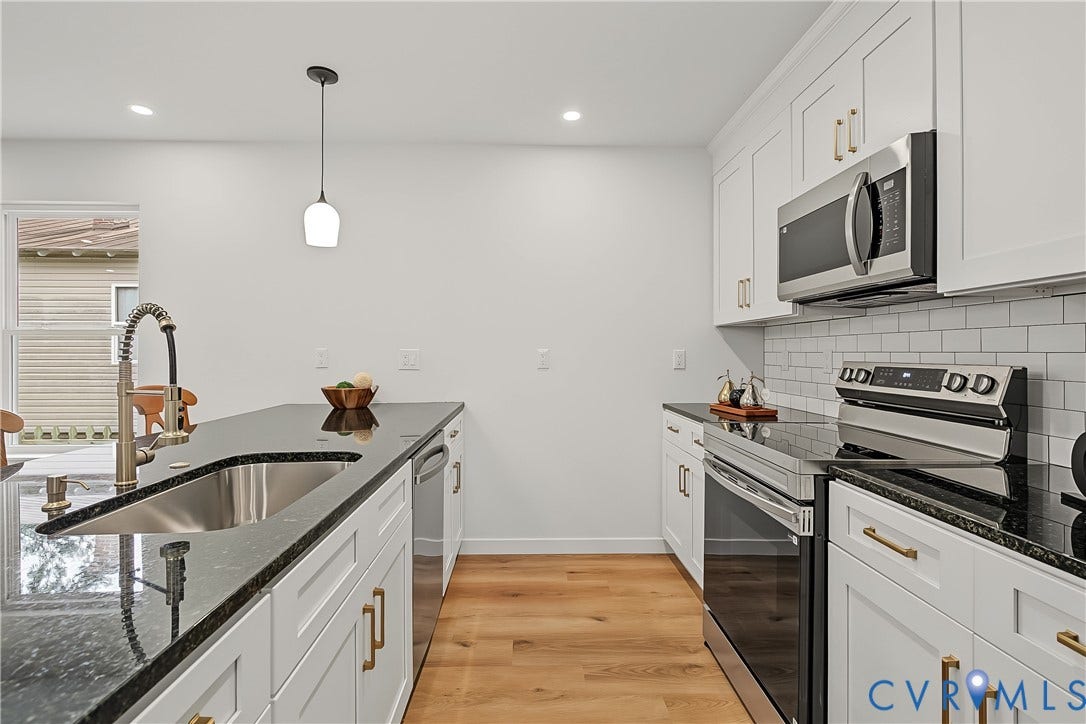 Modern kitchen featuring white cabinetry with gold-tone hardware, dark countertops, and stainless steel appliances