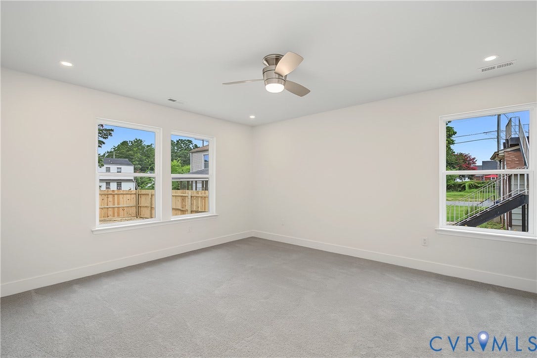 Bright and spacious secondary bedroom featuring neutral wall finishes, plush carpeting, a ceiling fan with integrated lighting, and multiple windows offering natural light and outdoor vistas