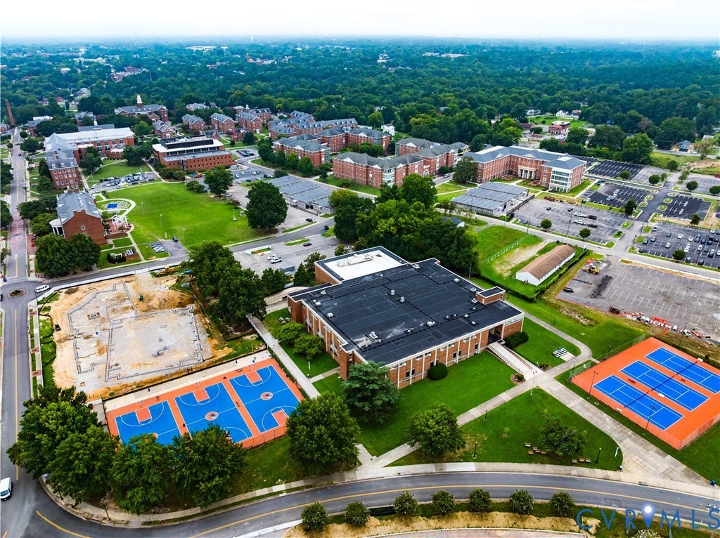 Aerial view of this institutional campus property showcasing multiple athletic courts with professional-grade surfacing in vibrant blue and orange, manicured lawn areas, a substantial brick academic building with dark roof, and surrounding residential neighborhoods
