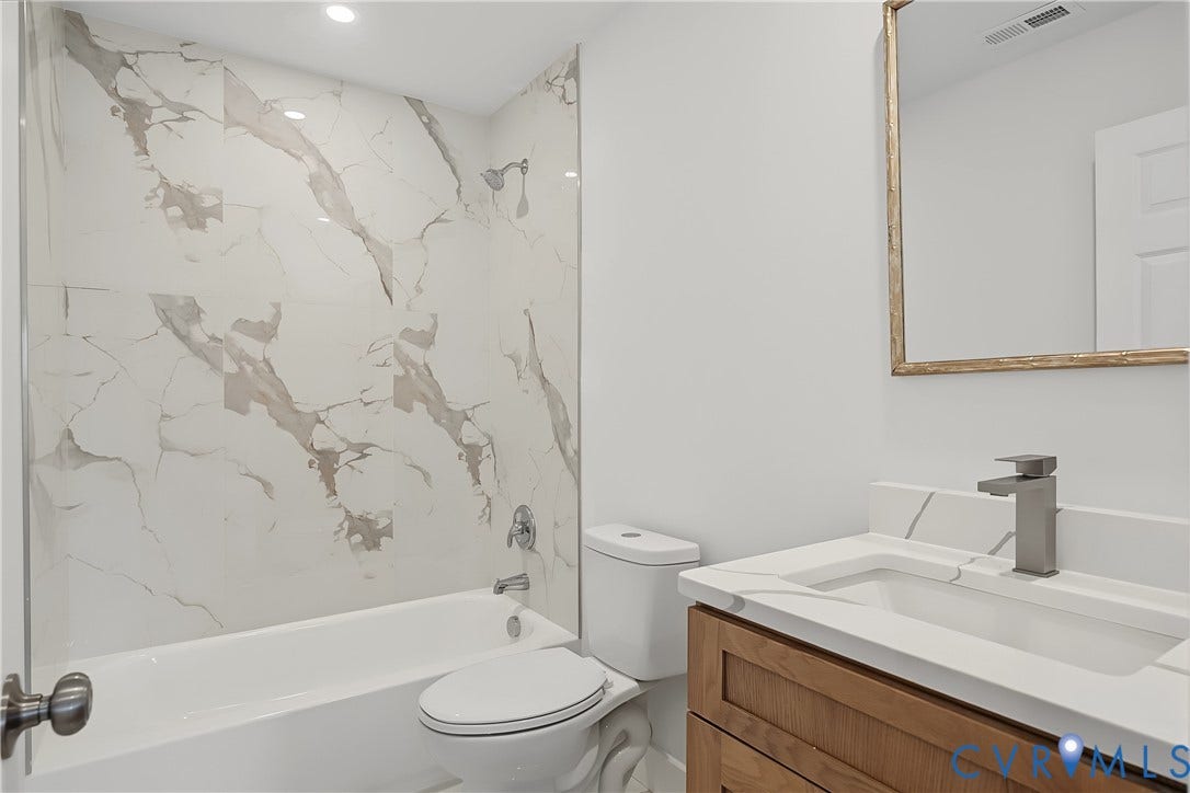 Bathroom featuring a white bathtub with a tile surround, a modern vanity with wood-finish cabinetry, a white countertop with integrated sink, and a brushed nickel faucet