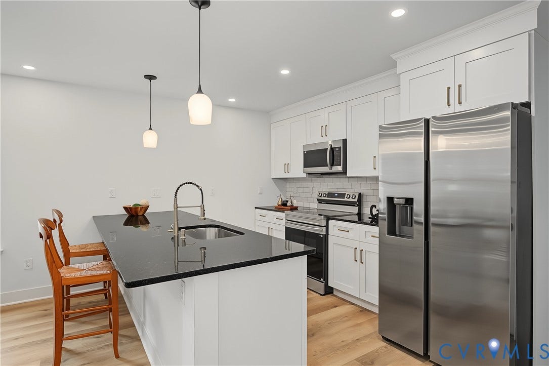 Modern kitchen featuring white shaker-style cabinetry with stainless steel hardware, black quartz countertops, and a waterfall-edge island