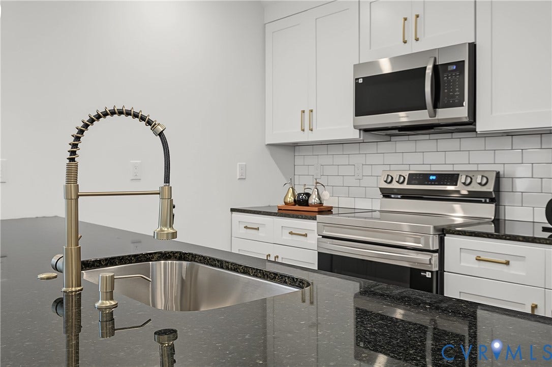 Modern kitchen featuring a sleek black granite countertop, stainless steel undermount sink, and a professional-grade spring-neck faucet in brushed gold finish