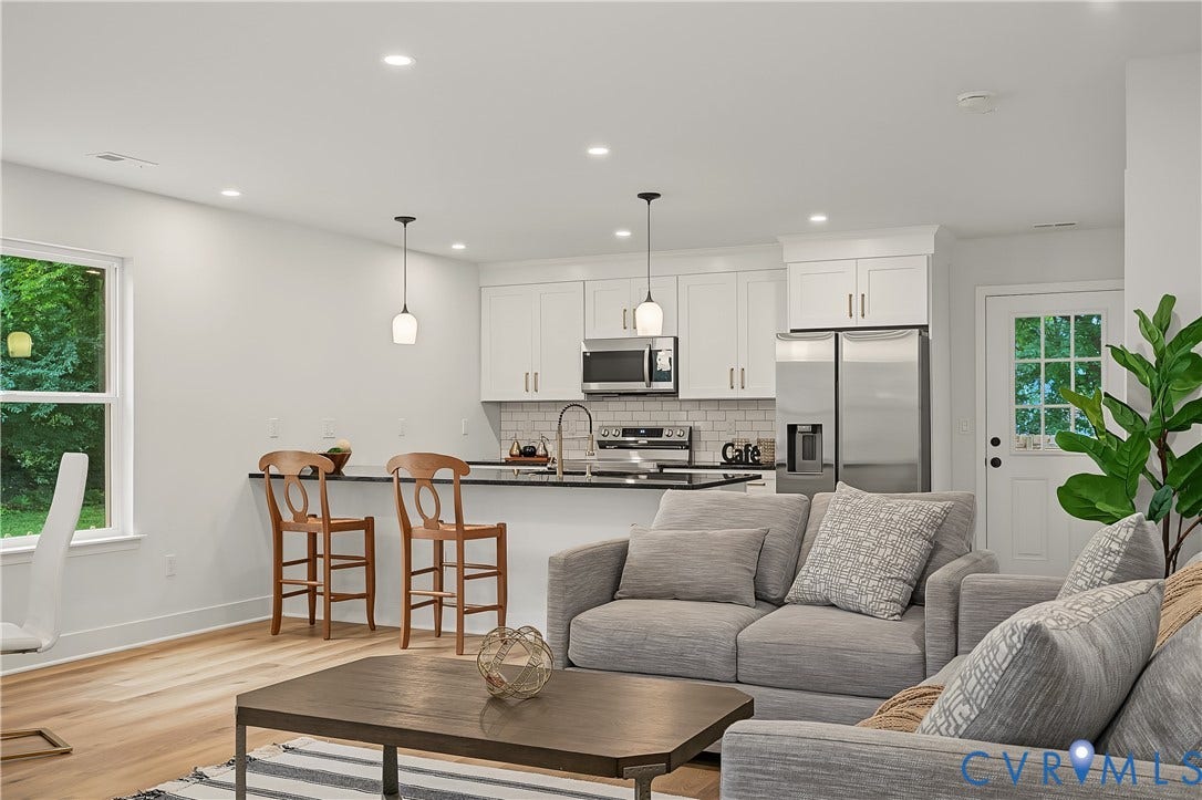 Open-concept living and kitchen featuring stainless steel appliances, white cabinetry with hardware accents, and a waterfall-edge island with seating for two