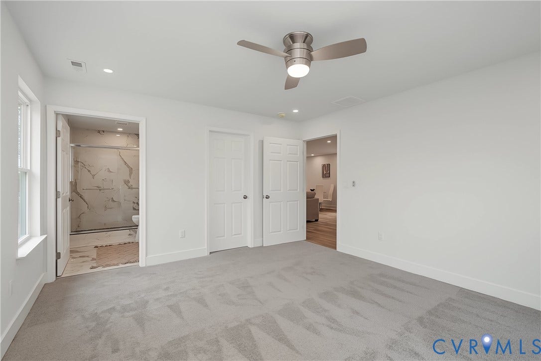 Spacious primary bedroom featuring neutral walls, plush carpet flooring with geometric pattern detail, and abundant natural light from dual windows