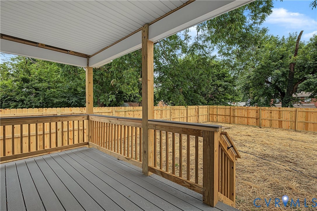 Covered porch with composite decking, wooden railings, and exposed beam ceiling overlooking a fenced yard with mature trees