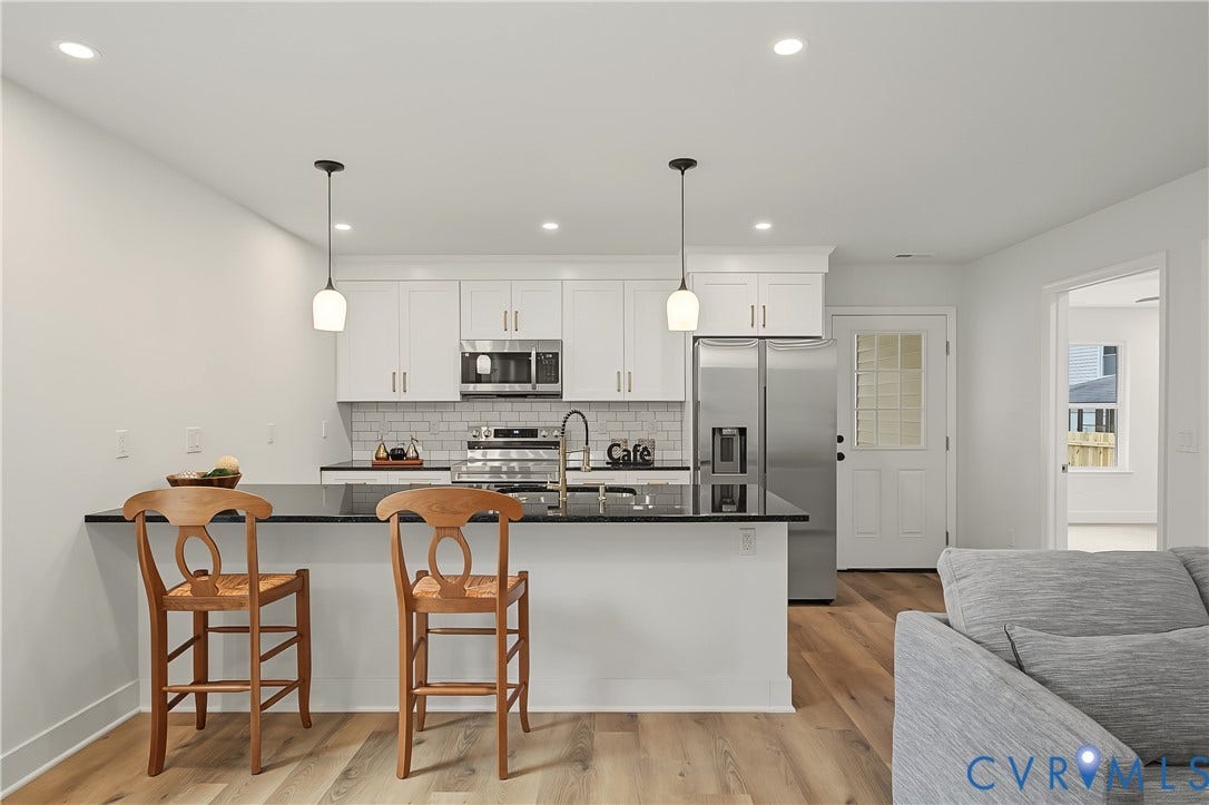 Modern kitchen featuring white cabinetry, stainless steel appliances, a black countertop island with pendant lighting, and wood-finish flooring