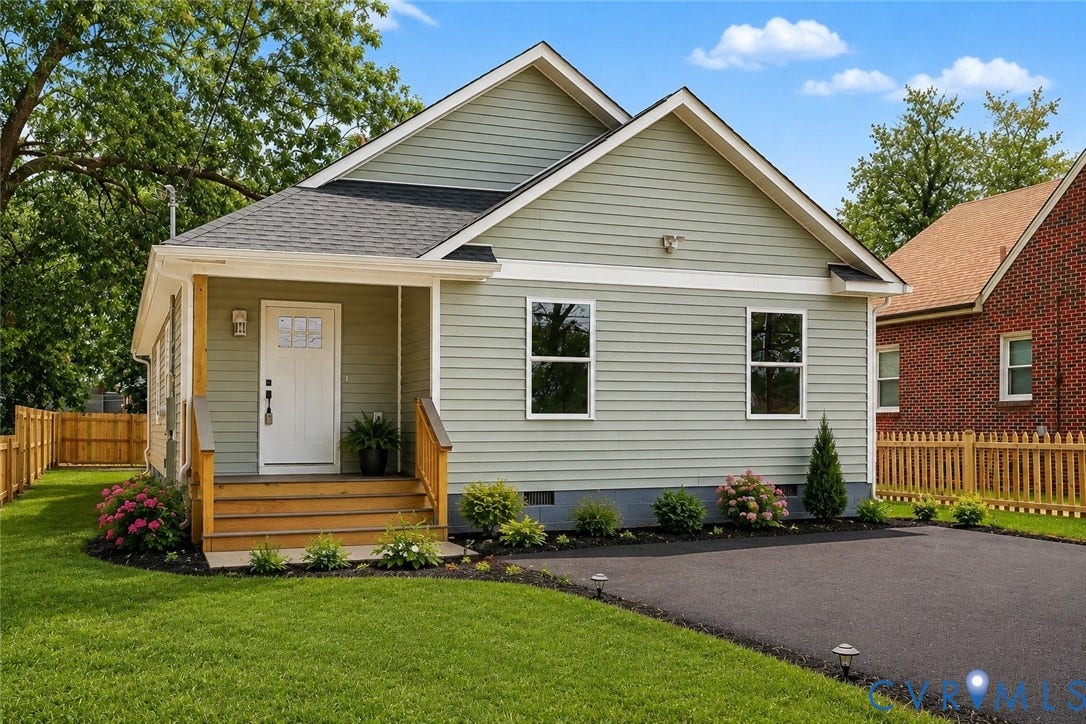 Exterior featuring light green horizontal siding, a covered front porch with wood stairs and railings, a white entry door with glass inserts, a paved driveway, and established landscaping