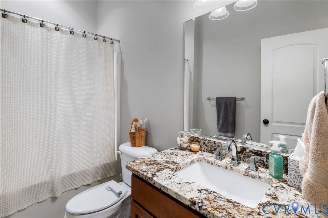 15918 Drumone Road, Hallsley, Midlothian, VA 23112 Bathroom featuring a wood-finish vanity with a stone countertop, an integrated sink with a chrome faucet, a large wall-mounted mirror, and a white toilet