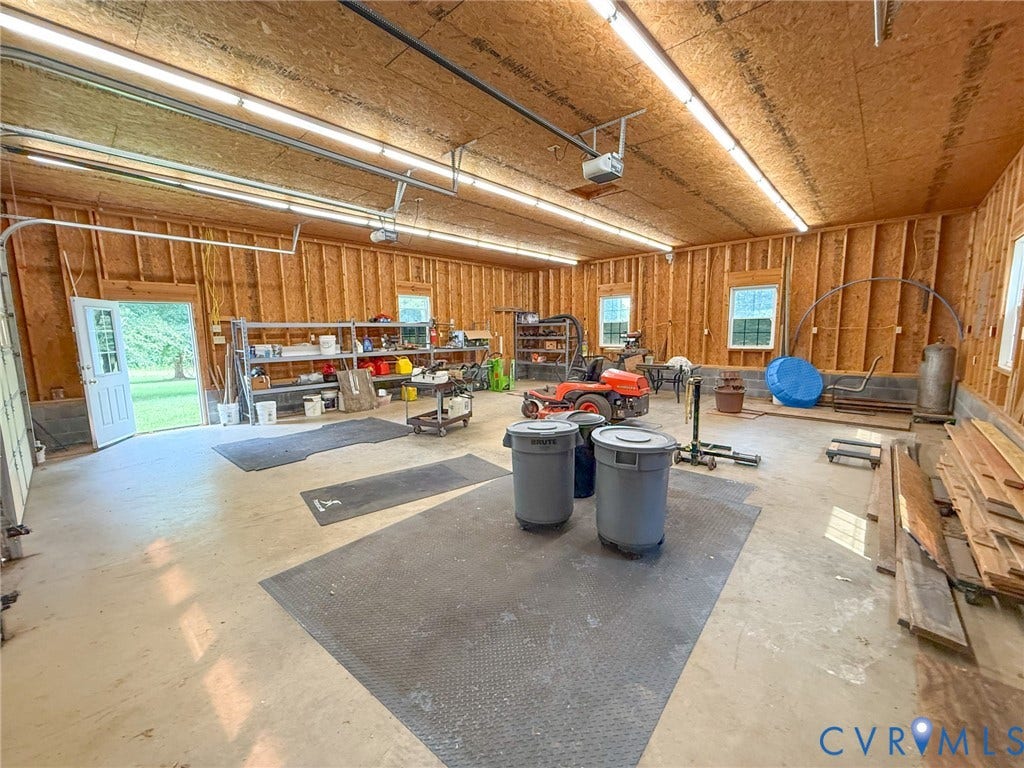 6688 Old Buckingham Road, Powhatan, VA 23139 Spacious garage featuring exposed wood framing, concrete flooring, multiple windows, and a side entry door