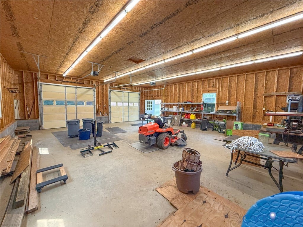 6688 Old Buckingham Road, Powhatan, VA 23139 Spacious utility building featuring two roll-up garage doors, exposed wood-frame construction, concrete flooring, and extensive overhead strip lighting