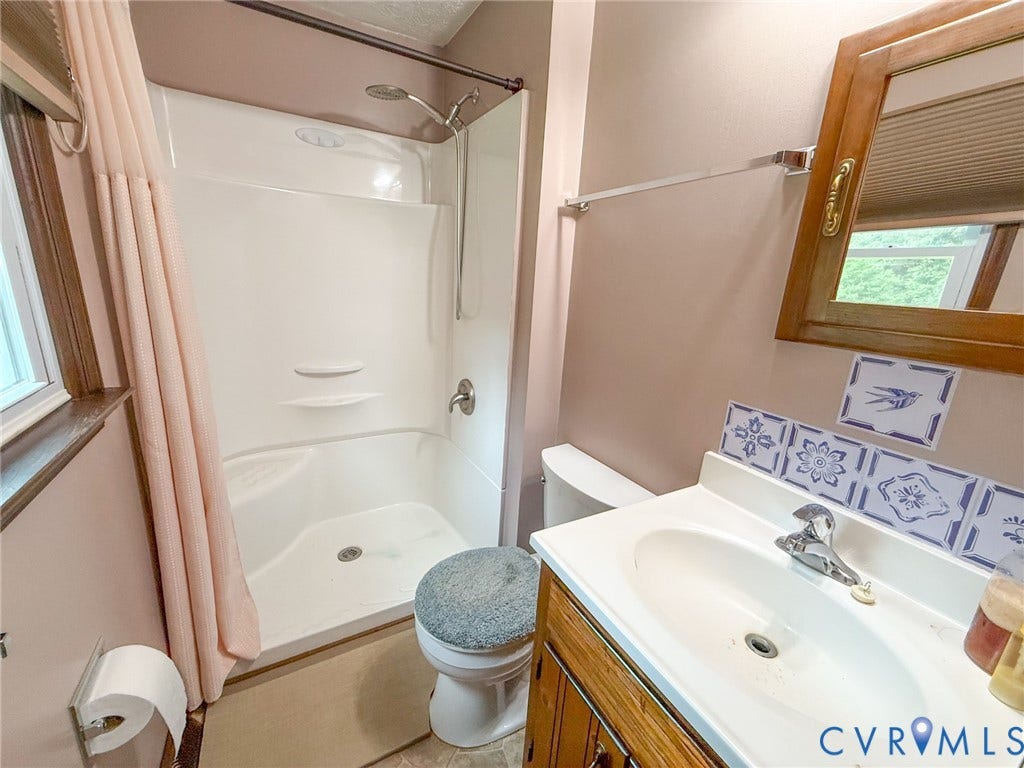 6688 Old Buckingham Road, Powhatan, VA 23139 Bathroom featuring a white integrated shower/tub unit, a vanity with a white countertop and basin sink, a wall-mounted mirror with a wood frame, and decorative blue and white tile accents
