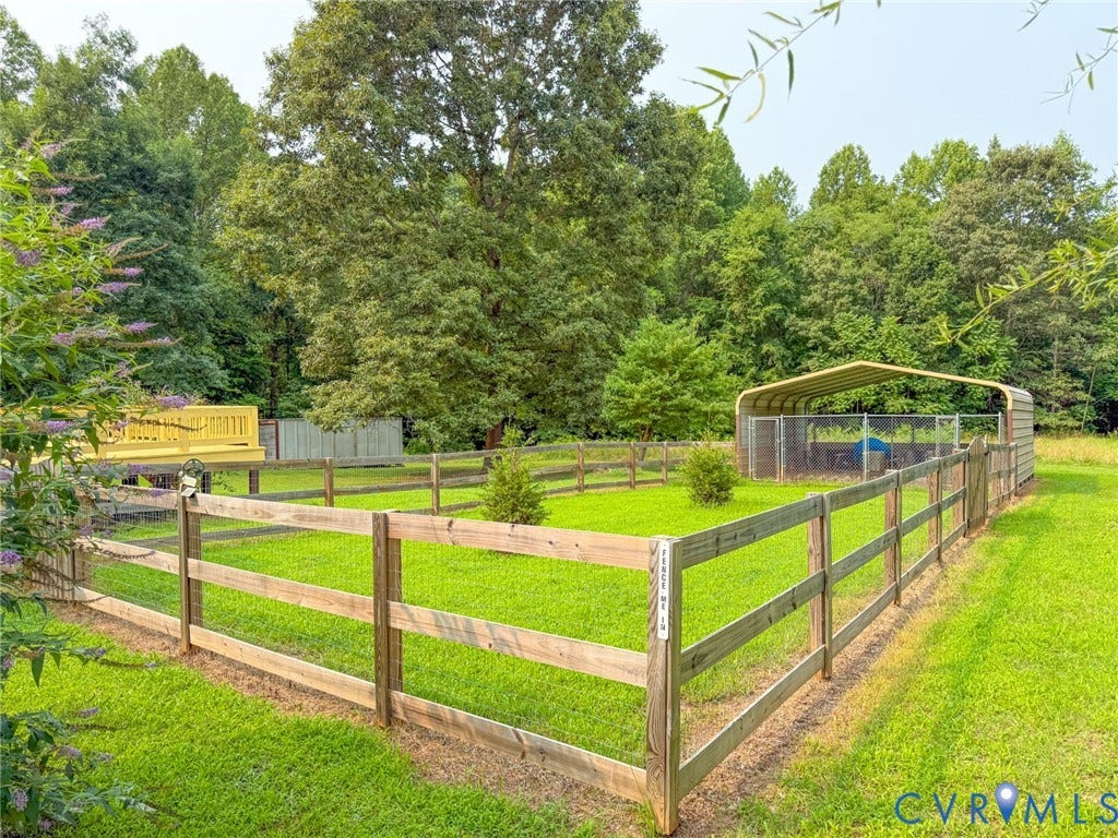 6688 Old Buckingham Road, Powhatan, VA 23139 Expansive fenced lawn area featuring a wooden split-rail fence, a raised wood deck, a metal carport, and a separate fenced enclosure