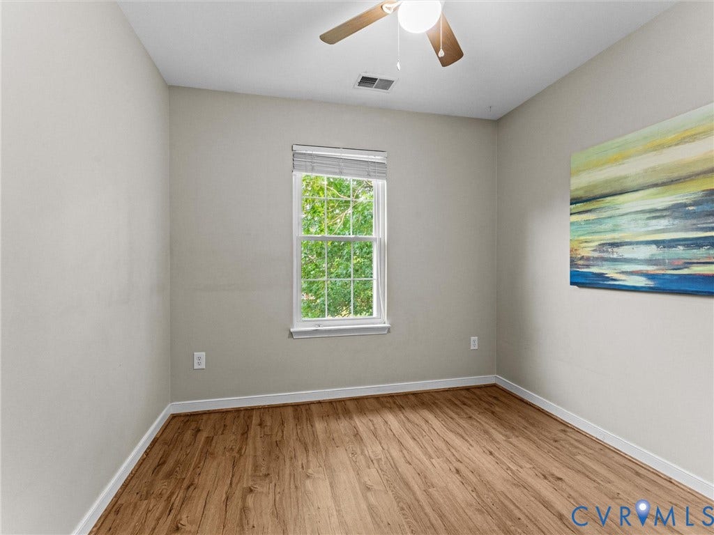 10100 Robin Lee Lane, Laurel Lakes, Glen Allen, VA 23060 Warm wood-finish flooring and neutral wall tones define this room, featuring a single double-hung window with privacy blinds, a ceiling fan with integrated lighting, and white trim throughout