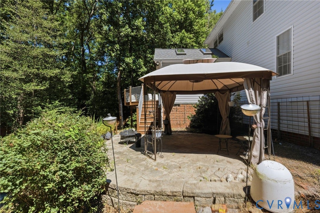 5215 Lippingham Lane, Stoney Glen West, Chester, VA 23831 Stone paver patio with a retaining wall, a multi-level deck with wood stairs and metal railings, and a lush, wooded perimeter