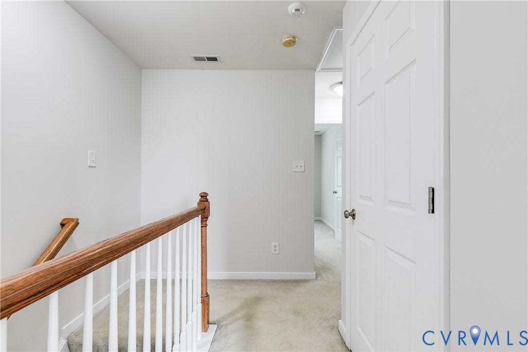 8004 Creekside Village Drive, Creekside Village, Mechanicsville, VA 23111 Upper-level hallway featuring light gray walls, carpet flooring, a white paneled door, and a wooden stair railing with white spindles