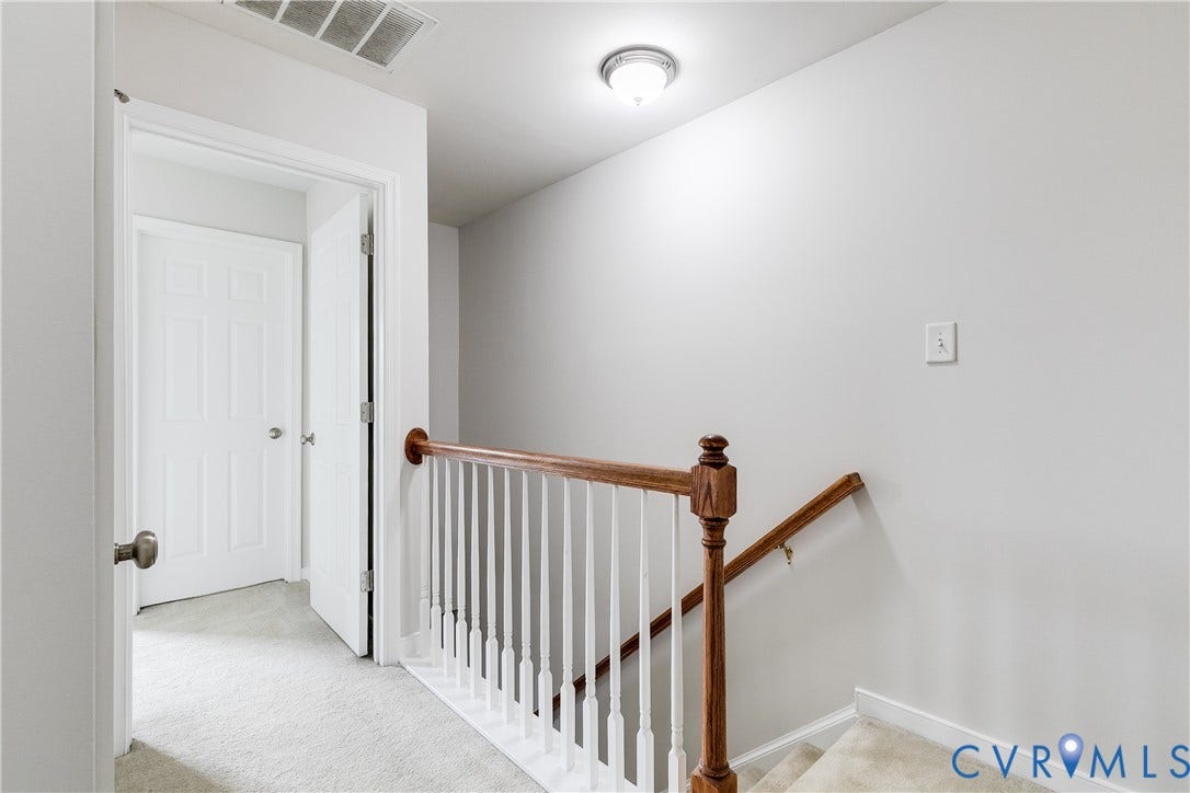 8004 Creekside Village Drive, Creekside Village, Mechanicsville, VA 23111 Carpeted hallway featuring a wooden banister with white balusters, leading to a paneled door