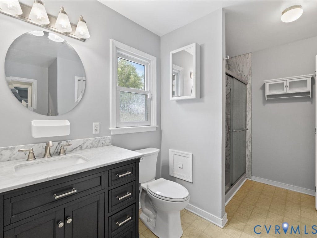 12230 Harrowgate Road, Chesterfield, VA 23831 Bathroom featuring a dark wood vanity with a white countertop and undermount sink, a round wall mirror, and a walk-in shower with a glass enclosure