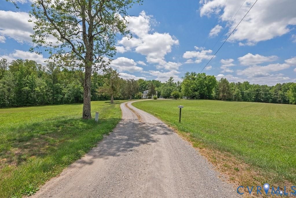 11300 Aspen Grove Drive, Glen Allen, VA 23059 Gravel driveway winding through expansive green lawns, bordered by mature trees and distant woodland