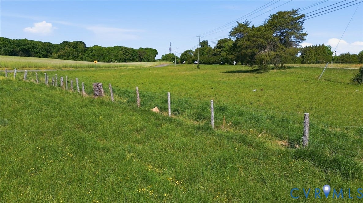 Expansive green acreage featuring a partial post fence line and distant mature trees