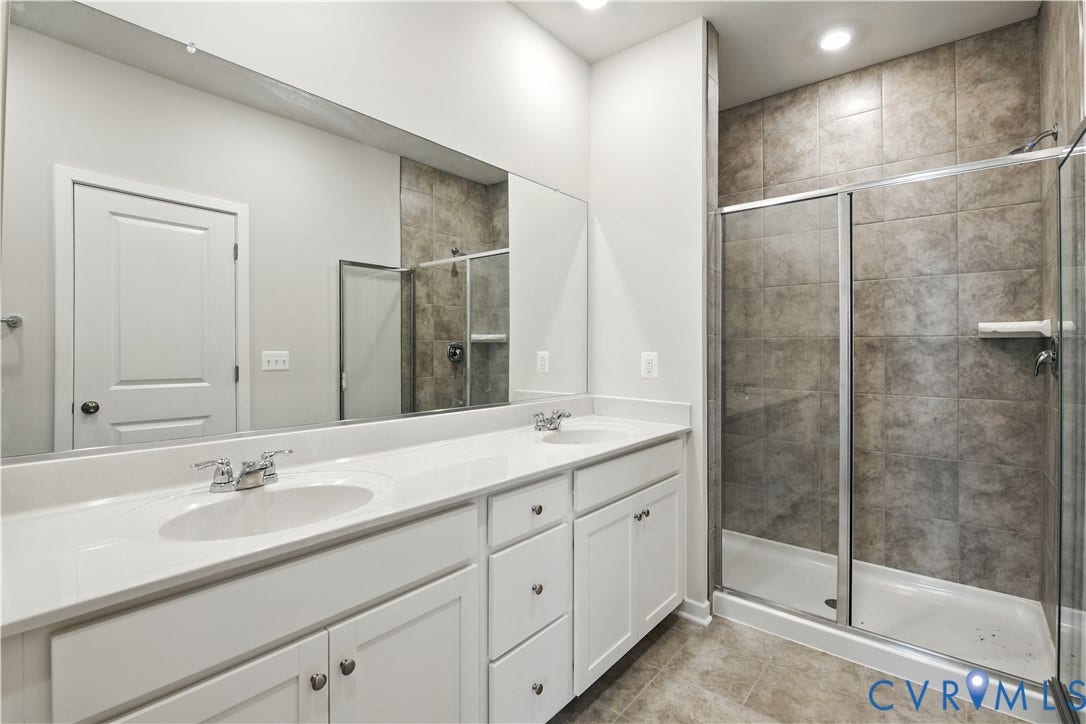 Double vanity with integrated sinks, white cabinetry, chrome fixtures, and a spacious walk-in shower featuring subway tile surround and a glass enclosure