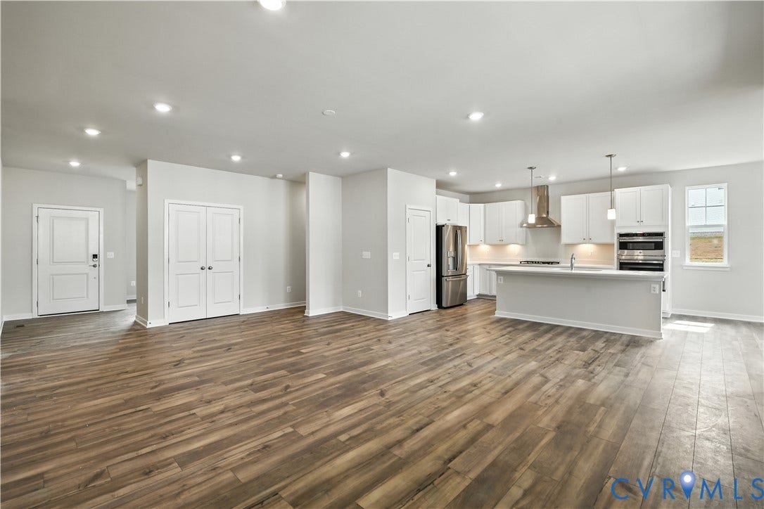Expansive living area with wood-finish flooring, recessed lighting, and a kitchen featuring white cabinetry, stainless steel appliances, and a central island