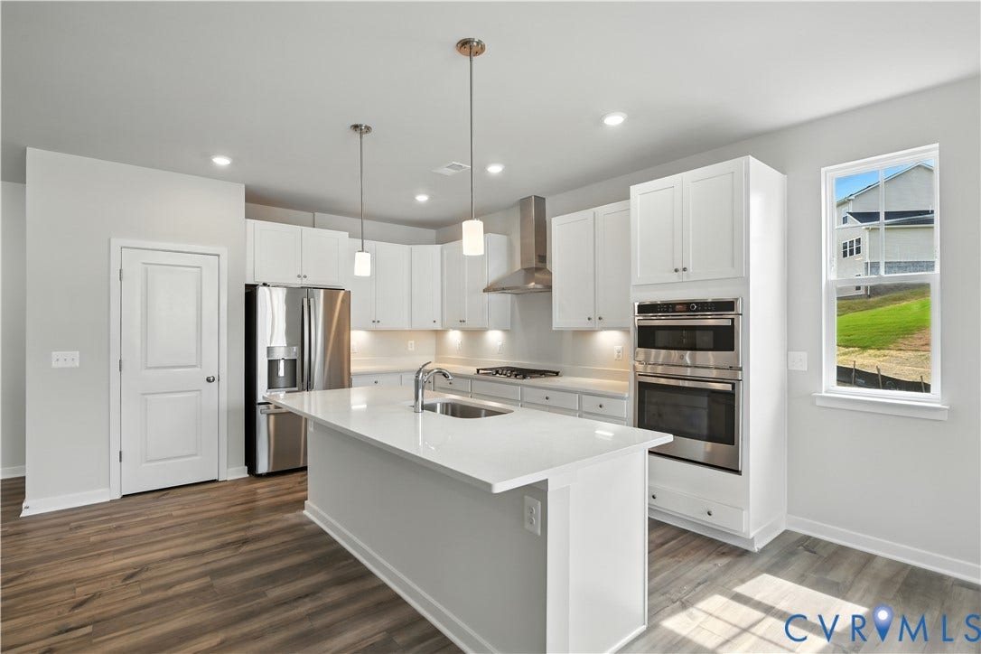 Modern kitchen featuring a central island with a sink, white cabinetry, stainless steel appliances, wood-finish flooring, and pendant lighting