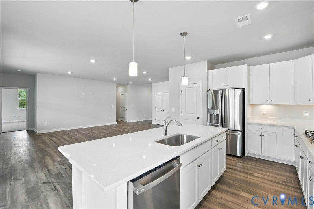 Contemporary kitchen featuring an island with a stainless steel sink, white cabinetry, integrated dishwasher, and stainless steel refrigerator