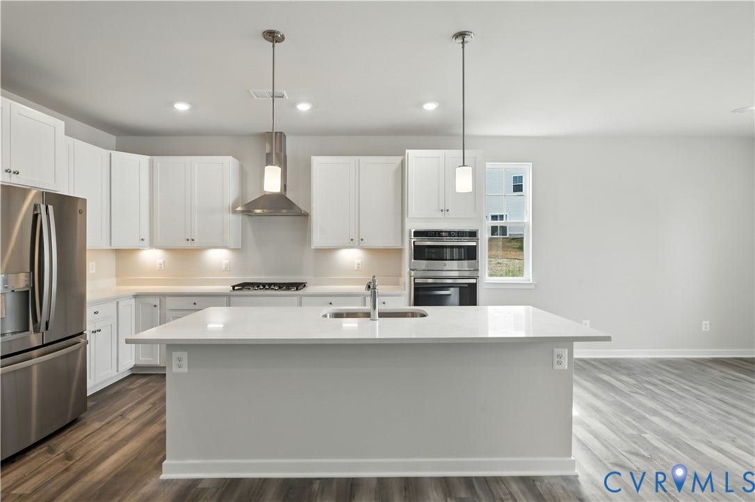 Contemporary kitchen featuring white cabinetry, stainless steel appliances, a center island with sink, pendant lighting, and wood-finish flooring