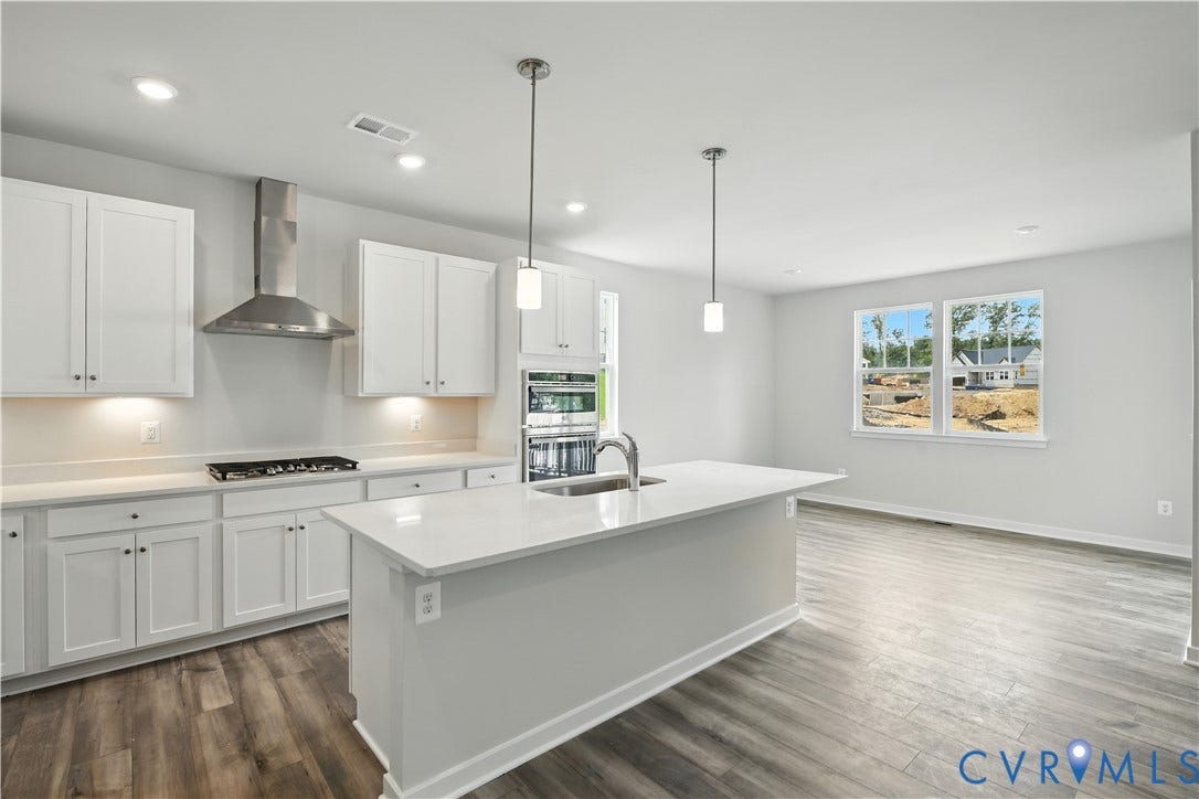 Modern kitchen featuring white shaker cabinetry, stainless steel appliances, a center island with sink and pendant lighting, and wood-finish flooring