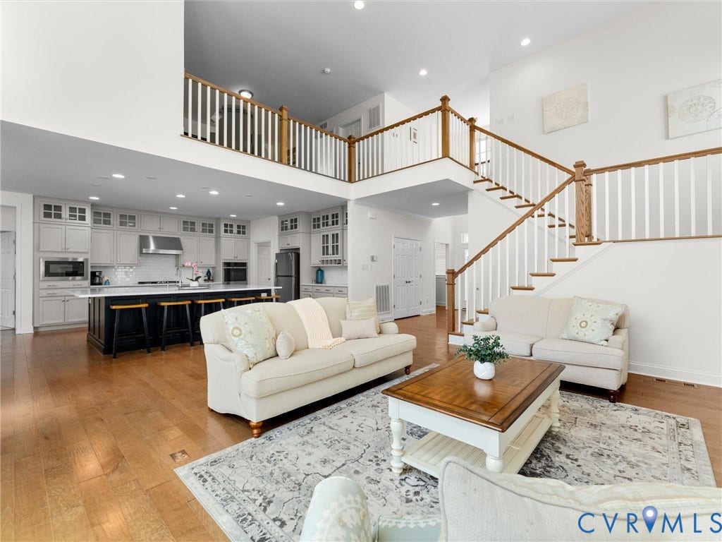 6642 Stonewolf Court, Moseley, VA 23120 Open-concept living area featuring hardwood flooring, a spacious kitchen island with seating, stainless steel appliances, a two-story ceiling, and a prominent staircase with wood railings