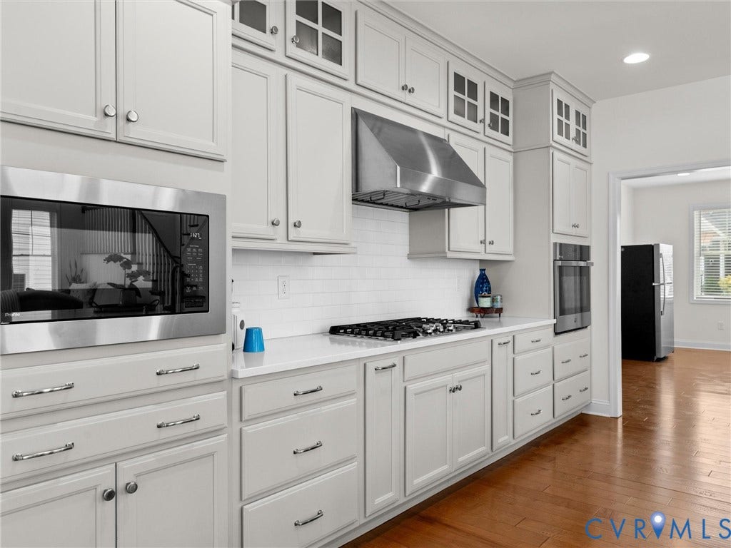 6642 Stonewolf Court, Moseley, VA 23120 Kitchen featuring light-toned cabinetry with glass-front accents, stainless steel appliances, a gas cooktop with a coordinating range hood, white subway tile backsplash, and wood-finish flooring