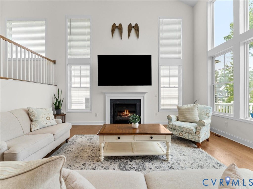 6642 Stonewolf Court, Moseley, VA 23120 Spacious living area featuring a fireplace with white mantel, a wall of tall windows, wood-finish flooring, and a white balustrade