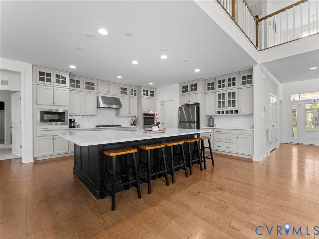 6642 Stonewolf Court, Moseley, VA 23120 Kitchen featuring light-toned cabinetry, a large center island with seating, stainless steel appliances, and wood-finish flooring