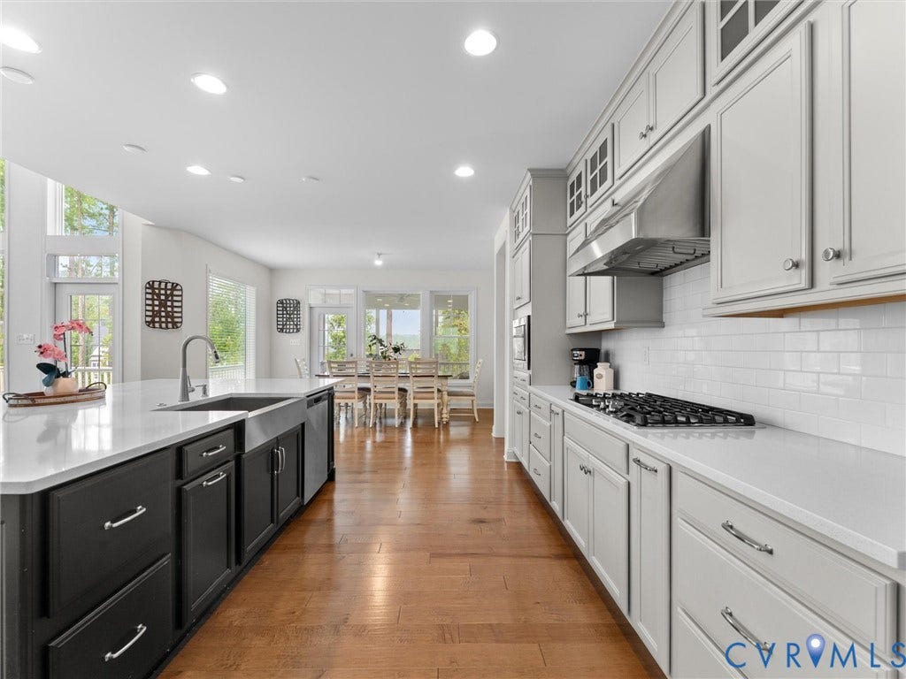 6642 Stonewolf Court, Moseley, VA 23120 Gourmet kitchen featuring a large central island with a farmhouse sink, light-toned countertops, hardwood flooring, gray shaker-style cabinetry, and a white subway tile backsplash