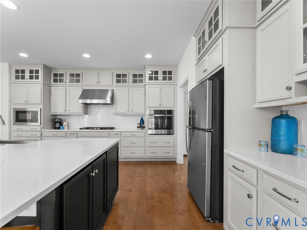 6642 Stonewolf Court, Moseley, VA 23120 Gourmet kitchen featuring a large island with a white countertop, extensive white cabinetry, stainless steel appliances, a white subway tile backsplash, and wood-finish flooring