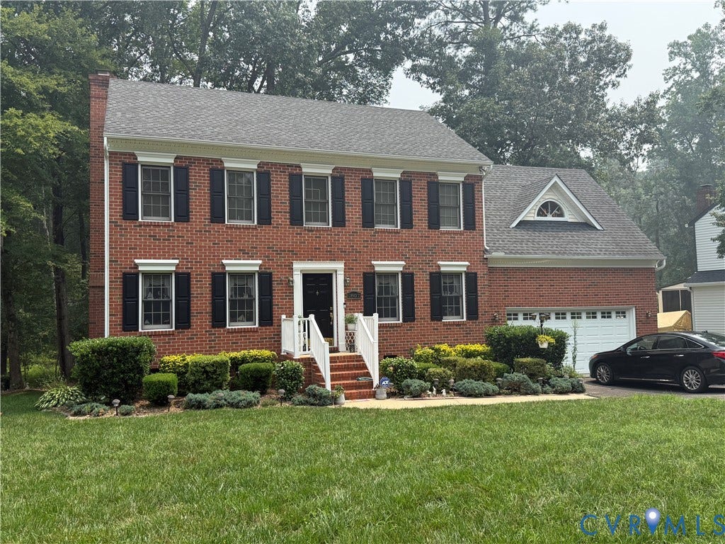 Brick exterior featuring black shutters, a two-car garage, and a dormer window