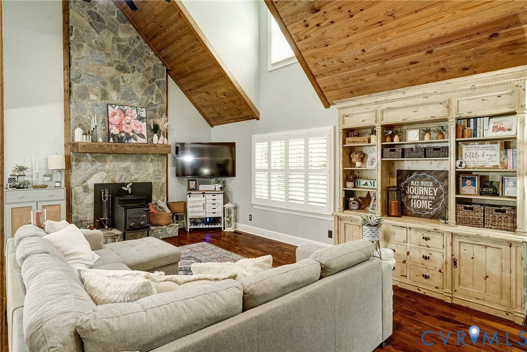 1174 Dorset Road, Powhatan, VA 23139 Spacious living area featuring a vaulted wood-paneled ceiling, a floor-to-ceiling stone fireplace with a wood mantel, wood-finish flooring, and built-in shelving with lower cabinetry