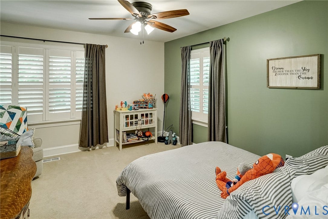 1174 Dorset Road, Powhatan, VA 23139 Carpeted room featuring a ceiling fan with wood-finish blades, two windows with white plantation shutters, and a two-tone paint scheme