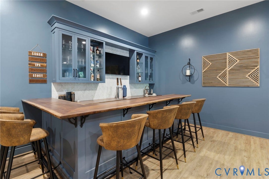 1925 Muswell Court, Hallsley, Midlothian, VA 23112 Custom built-in bar featuring a wood-finish countertop, under-cabinet lighting, glass-front upper cabinetry, and a textured backsplash