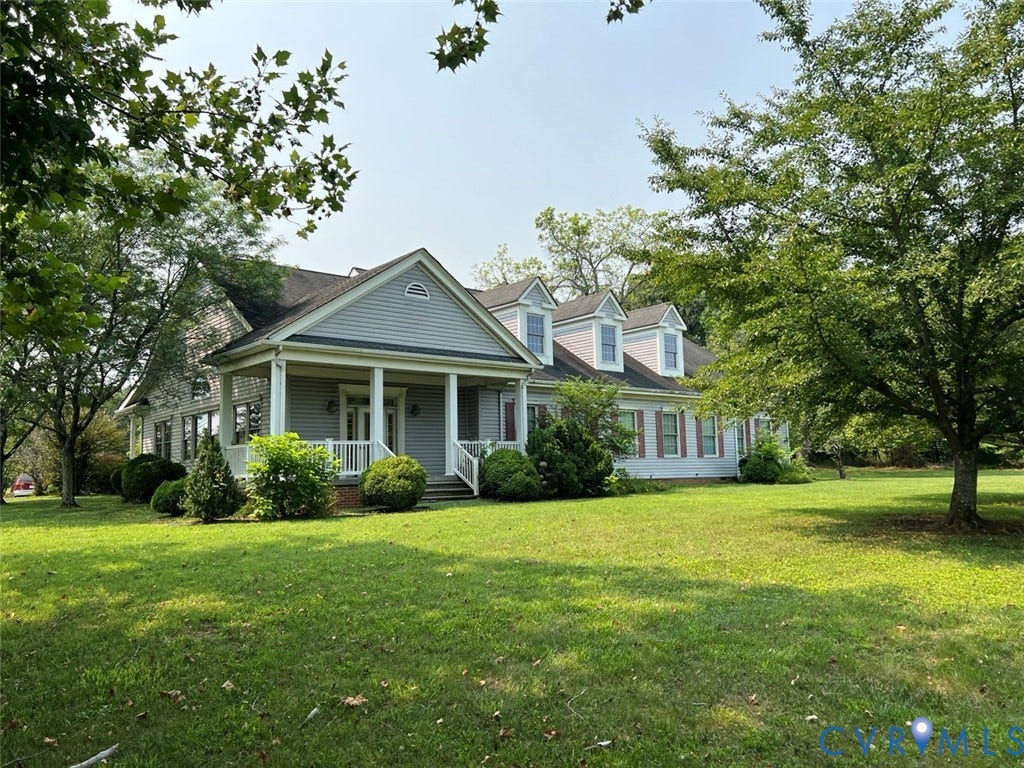 4064 James Madison Highway, Fork Union, VA 23055 Expansive property featuring a grey siding exterior, a welcoming front porch with white railings, multiple dormer windows, and mature trees surrounding a large lawn