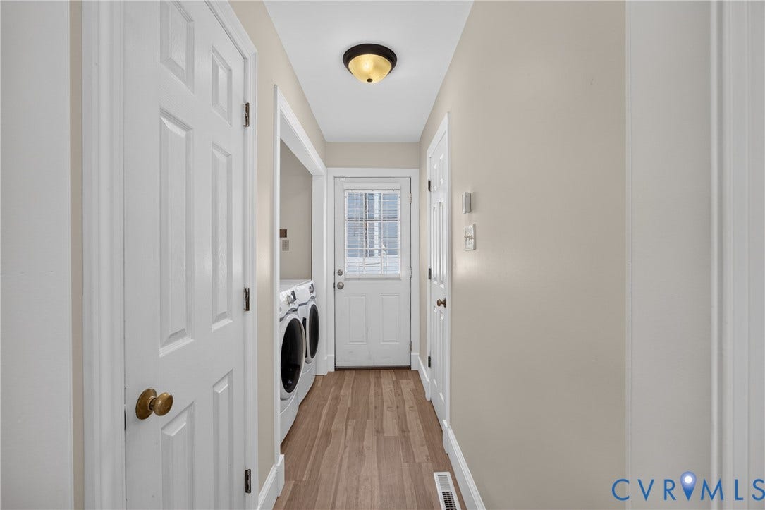 8436 Sir Lionel Place, Kingsland Wood, Ampthill, VA 23237 Bright laundry hallway featuring wood-finish flooring, white six-panel closet doors with brass hardware, a ceiling-mounted light fixture, and direct access to an exterior door with multiple storage closets lining the passage
