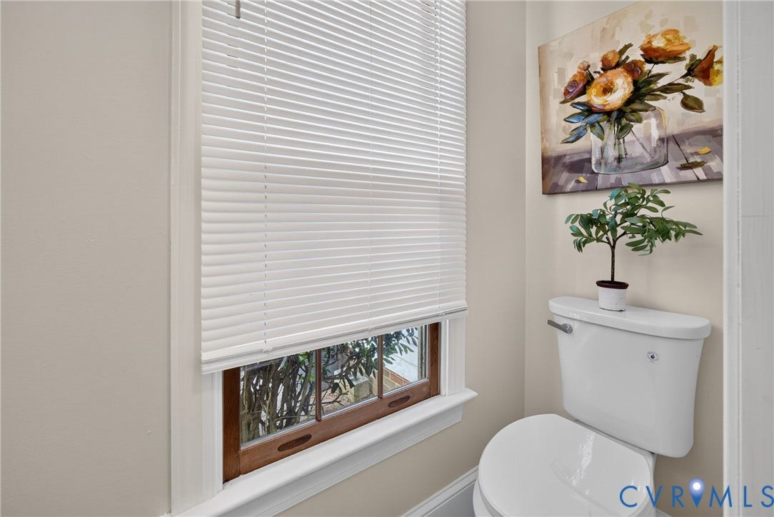 8436 Sir Lionel Place, Kingsland Wood, Ampthill, VA 23237 White toilet with a built-in flush handle, a window with wood-finish trim, and white horizontal blinds