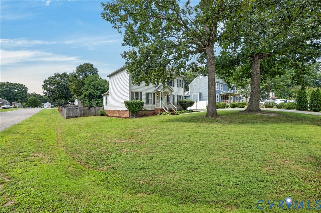 8436 Sir Lionel Place, Kingsland Wood, Ampthill, VA 23237 Two-story home with white siding and dark shutters, featuring a front porch with white railings, a brick foundation, and mature trees in the front yard