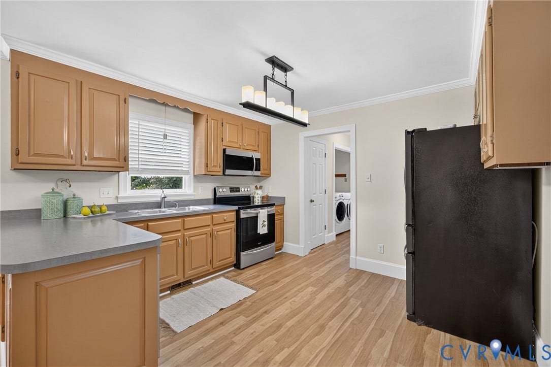 8436 Sir Lionel Place, Kingsland Wood, Ampthill, VA 23237 Spacious kitchen featuring wood cabinetry, stainless steel appliances including a gas range and microwave, gray countertops, wood-finish flooring throughout, and abundant natural light from a window over the sink