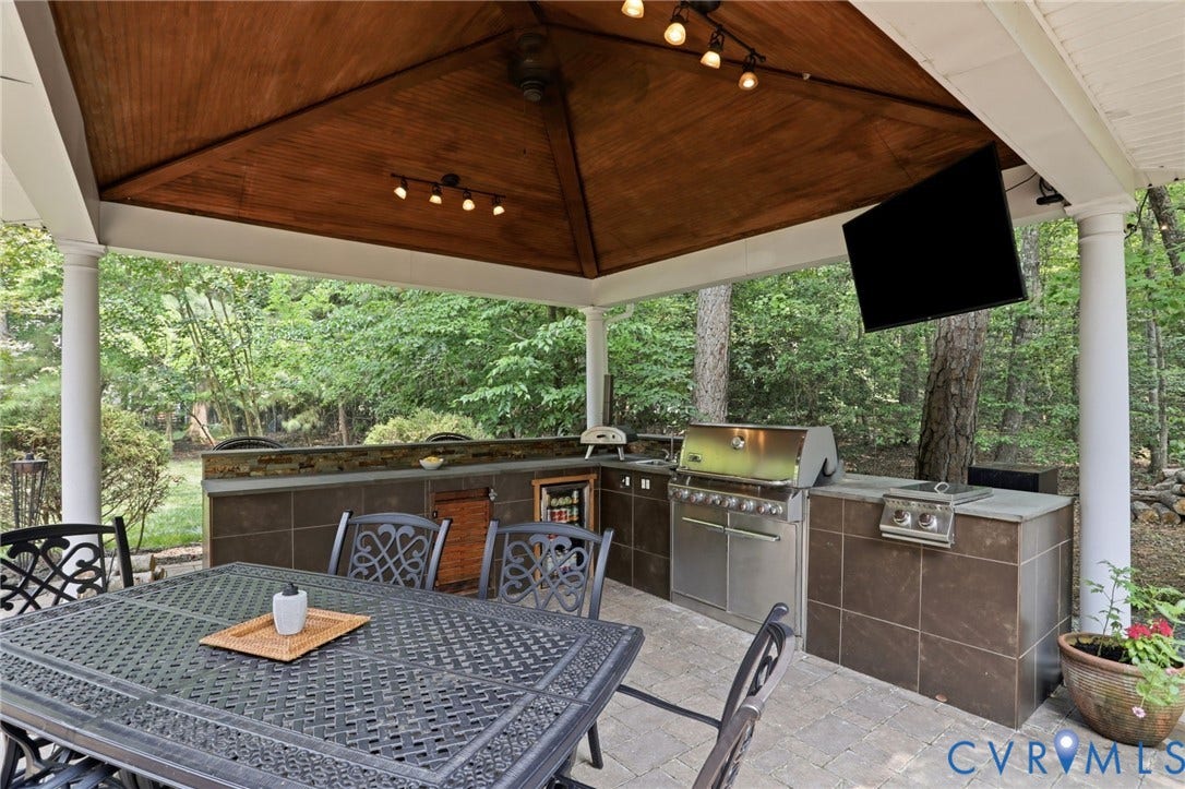 3655 Stone Harbor Drive, Midlothian, VA 23113 Covered patio featuring a wood-finish vaulted ceiling with track lighting, an outdoor kitchen with integrated stainless steel appliances, a mounted exterior display, and a paver patio surface