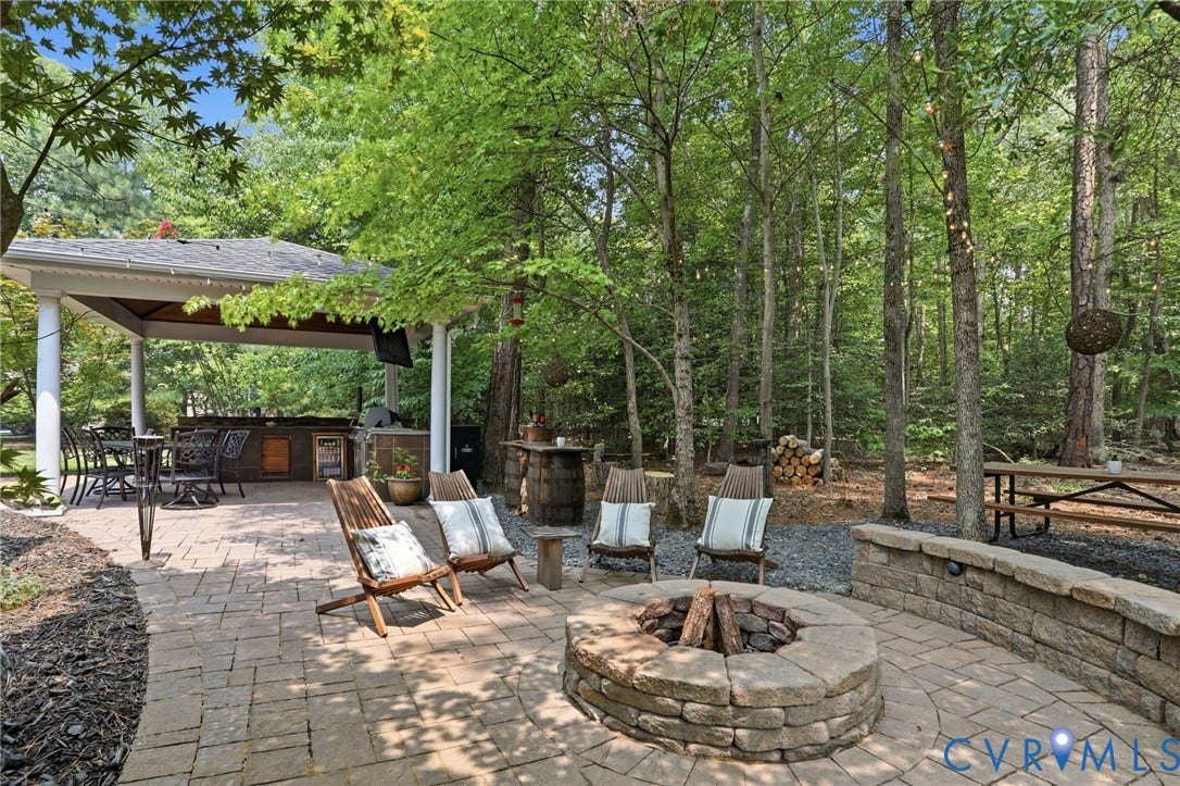 3655 Stone Harbor Drive, Midlothian, VA 23113 Expansive paver patio featuring a stone fire pit, a stone retaining wall, and a covered outdoor entertaining area with a built-in outdoor kitchen