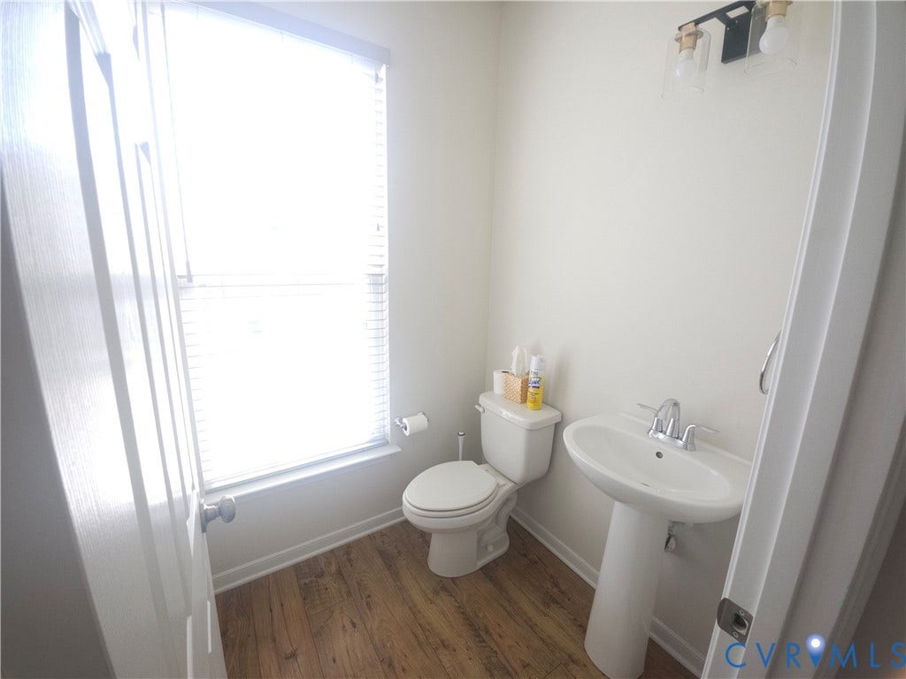 11304 Magill Terrace Drive, Chester, VA 23831 Bright, light-filled bathroom featuring a pedestal sink with chrome fixtures, a low-profile toilet with dual-flush capability, wood-finish flooring, and a large window with natural light