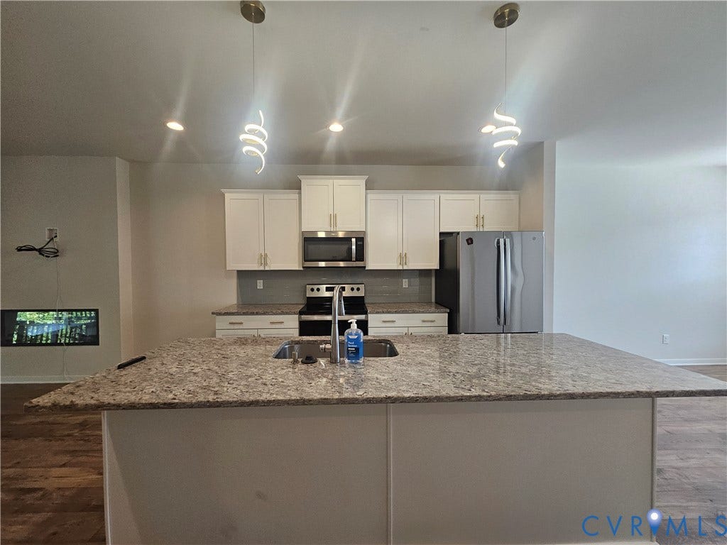 11304 Magill Terrace Drive, Chester, VA 23831 Modern kitchen featuring a large granite-topped island with seating, stainless steel appliances including dual wall ovens, cream cabinetry with brushed nickel hardware, and a spacious open floor plan