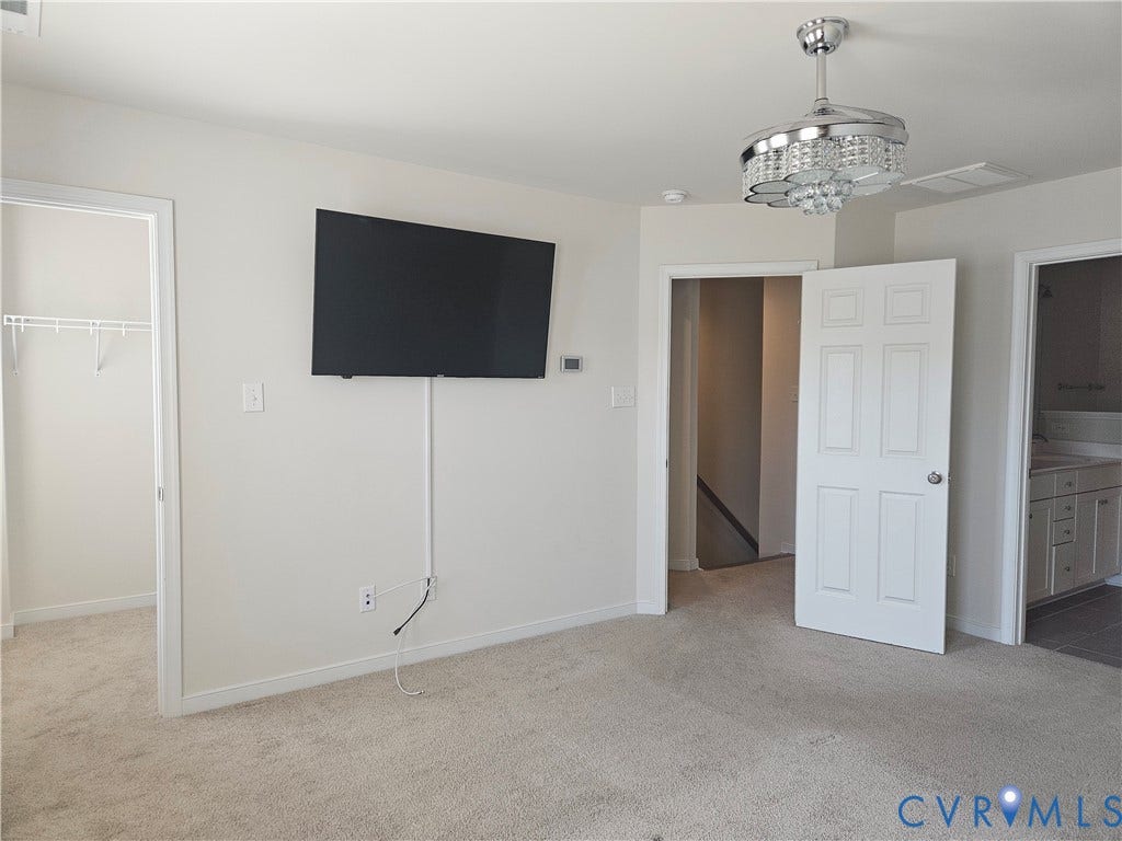 11304 Magill Terrace Drive, Chester, VA 23831 Spacious primary living area with neutral carpet flooring, wall-mounted flat-screen television with concealed wiring, decorative pendant lighting fixture, and multiple white six-panel doors providing access to adjoining rooms and closet storage