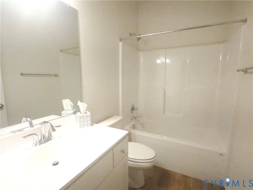 11304 Magill Terrace Drive, Chester, VA 23831 White vanity with integrated sink, chrome faucet, wall-mounted mirror, white bathtub with shower, and wood-finish flooring
